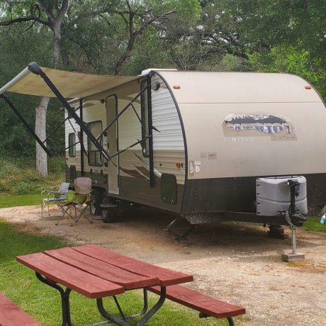 Travel Trailer backed into an RV site with a picnic table in the yard.